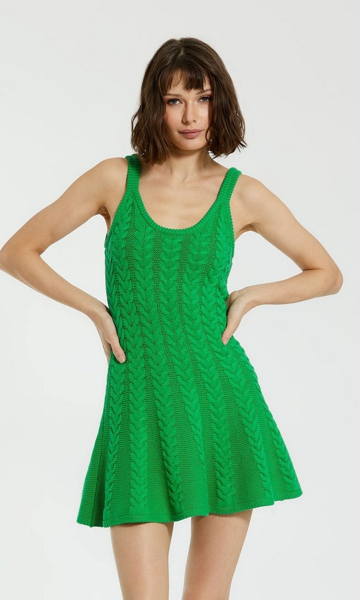 A woman with short brown hair wears the Designer Short Knit Dress K12004 by Mac Duggal—a sleeveless, bright green chunky knit dress with a flared skirt—while standing against a plain light background.